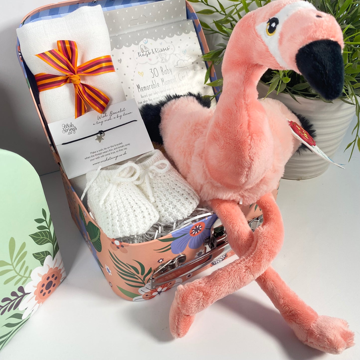 A baby keepsake case containing a Keeleco Flamingo baby soft toy, a packet of baby milestone cards, a new mum wish bracelet,and a large white baby muslin square complete this baby gift hamper.