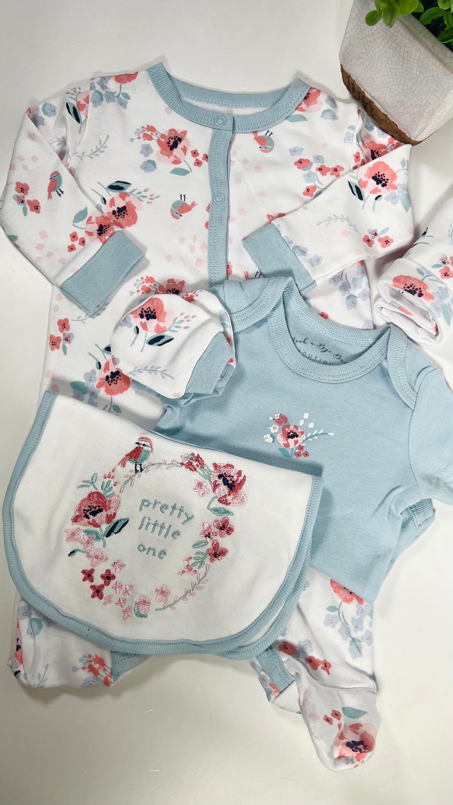 a 6 piece baby clothing set on white with a blue and pink floral pattern with birds and a blue trim. A matching baby bib, baby vest, hat and scratch mitts.
