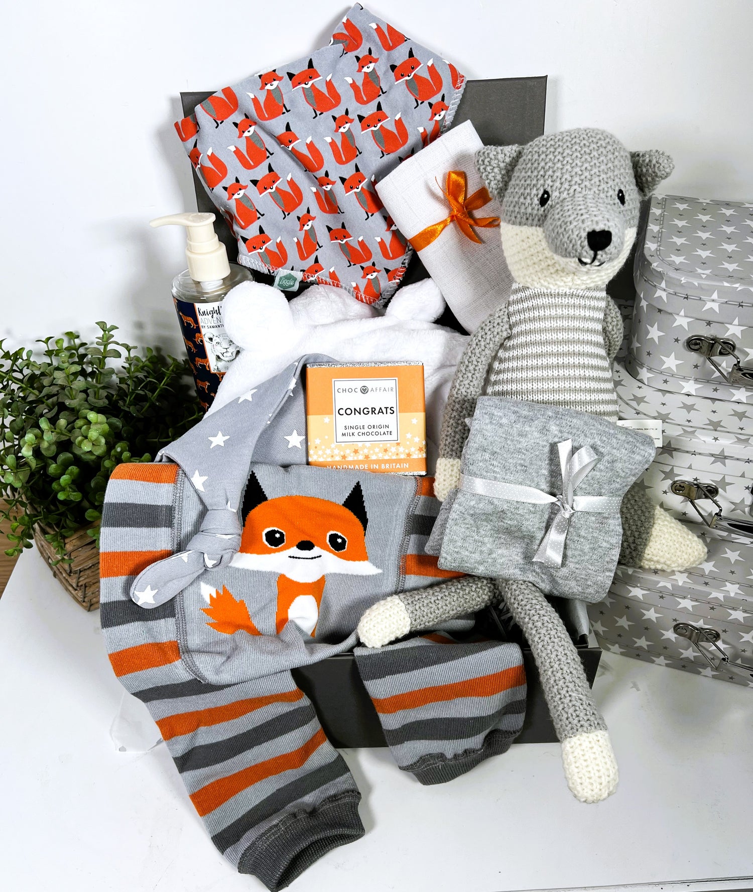  A fox themed new baby hamper containing a wilbeery fox knitted toy, a pair of Ziggle fox baby leggings with a Ziggle fox bib, a white hooded baby dressing gown, a bottle of baby wash, a Ziggle grey and white stars baby knot hat, a muslin square a grey baby vest and a bar of chocolate.